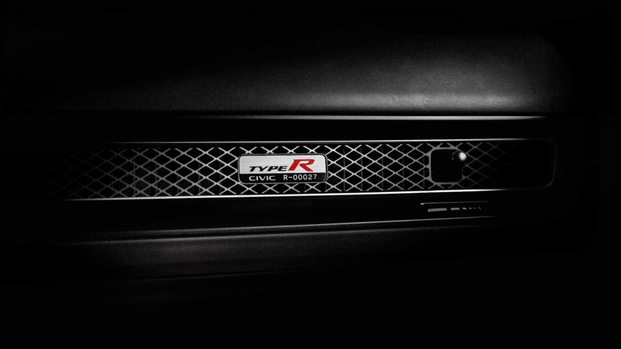 Front grille of a Honda Civic Type R with a metal lattice pattern and a centered Type R badge, in low lighting.
