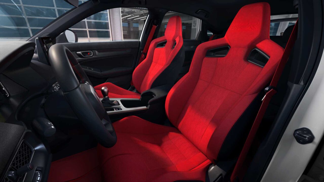 Red sporty car seats in a dark interior, front passenger and driver seats visible with center console and gear shifter nearby