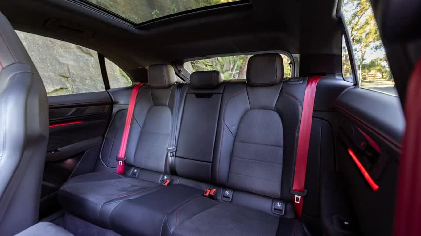 Back seat of a modern car with black leather upholstery and red seat belts, seen through a panoramic sunroof overhead.