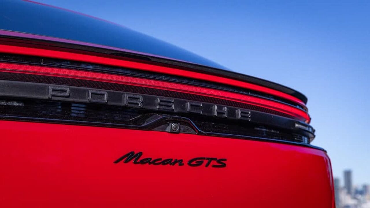 Rear end of a red Porsche Macan GTS showing the Porsche lettering and taillight against a blue sky.