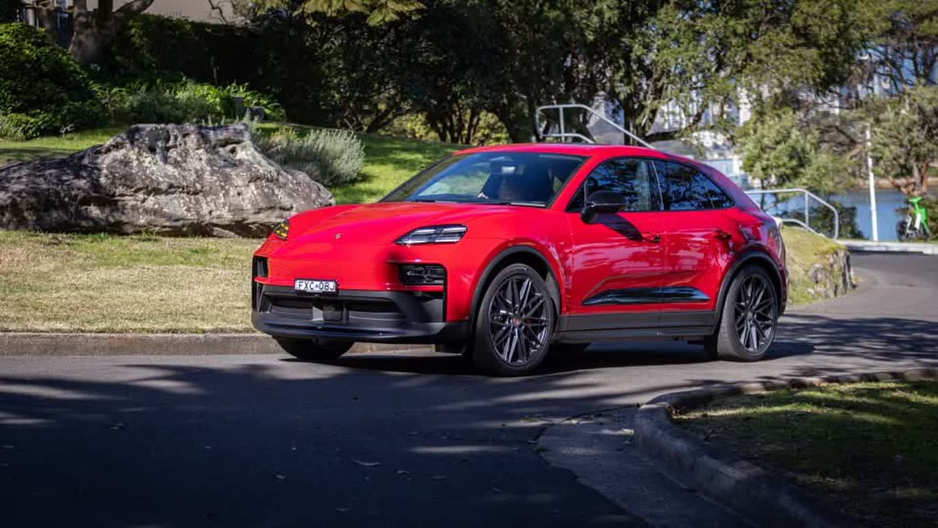 Red Porsche SUV parked on a suburban street with greenery and rocks in the background.