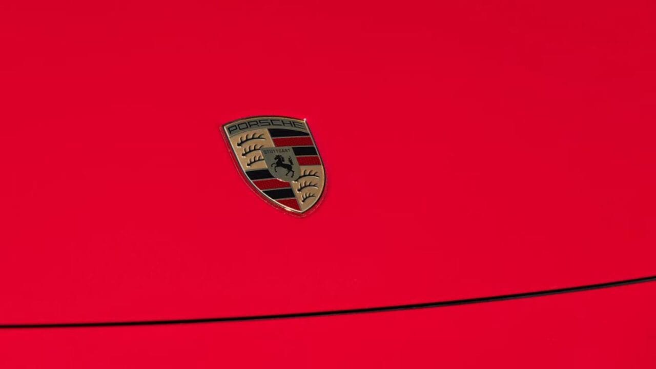 Porsche shield logo on a bright red car surface with a black curved line nearby