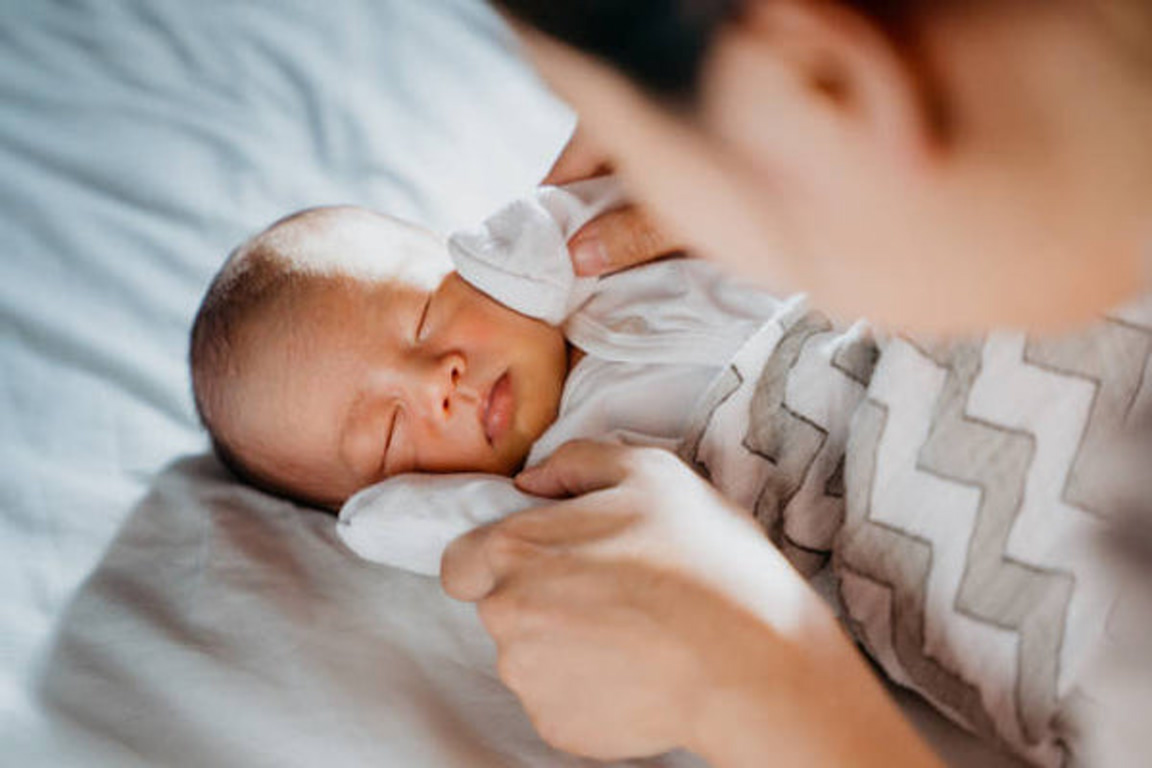 Newborn baby sleeping on a soft blanket with a caregiver's hands nearby.