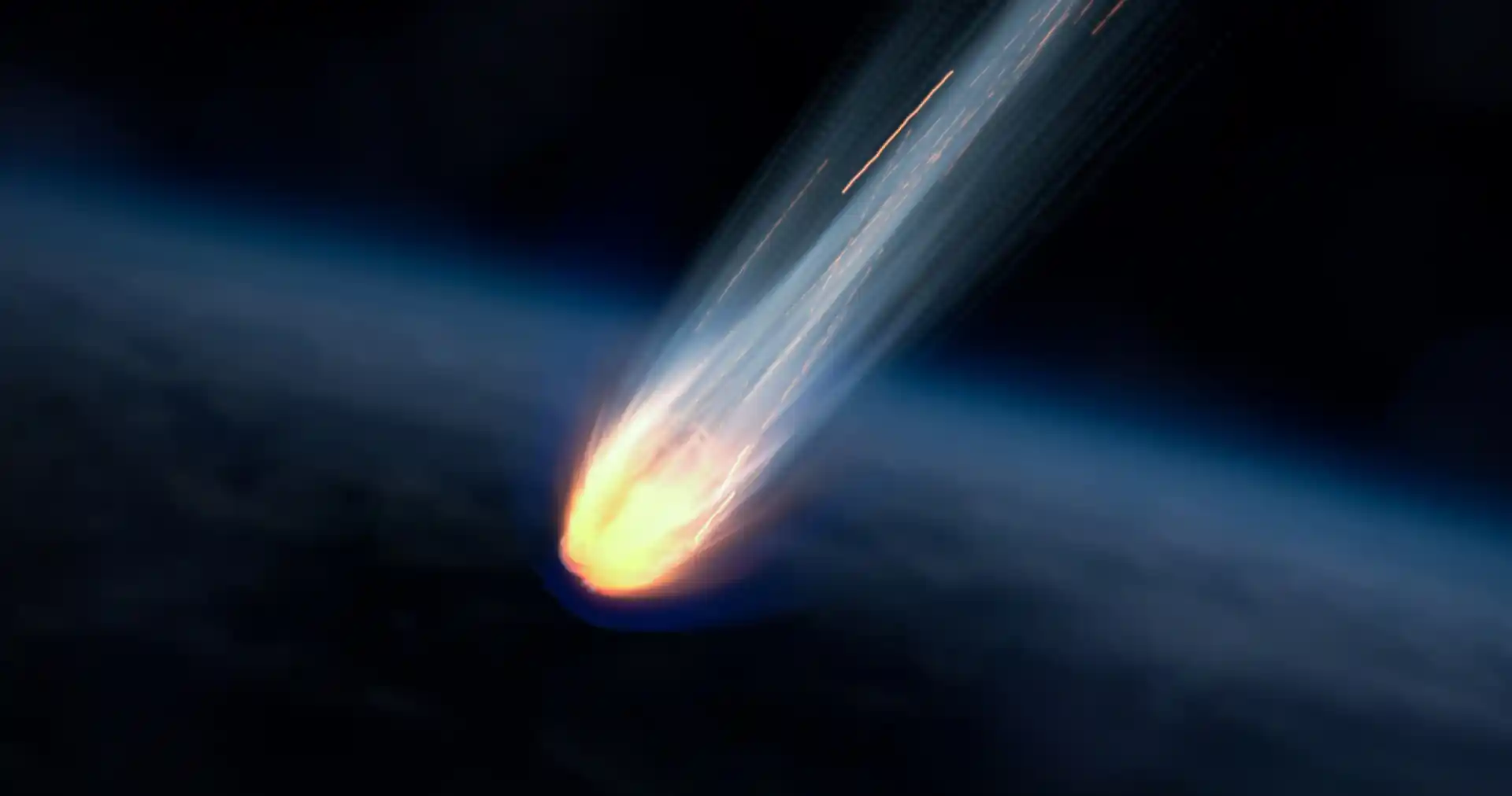 Bright fireball streaking across a dark night sky with a glowing fiery tail and blue atmospheric glow behind it.