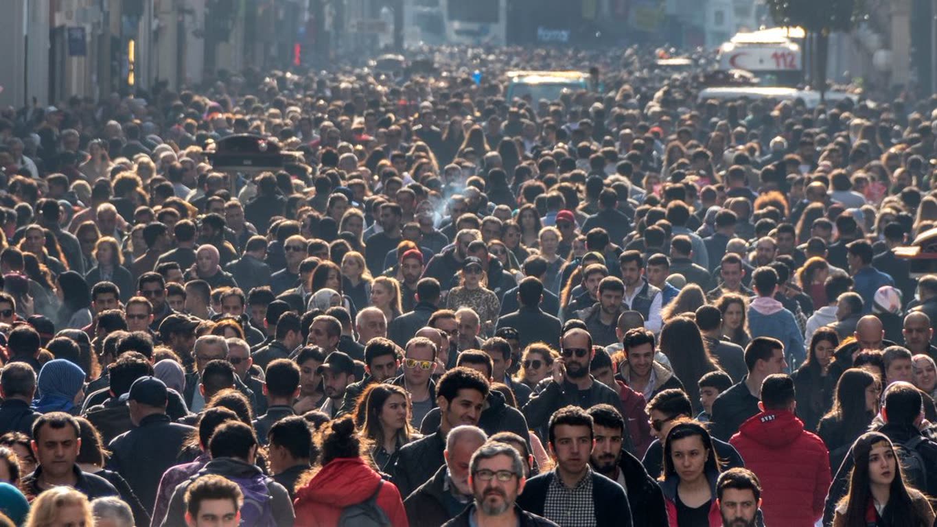 Dense crowd of pedestrians filling a city street during daytime as seen from mid-block.