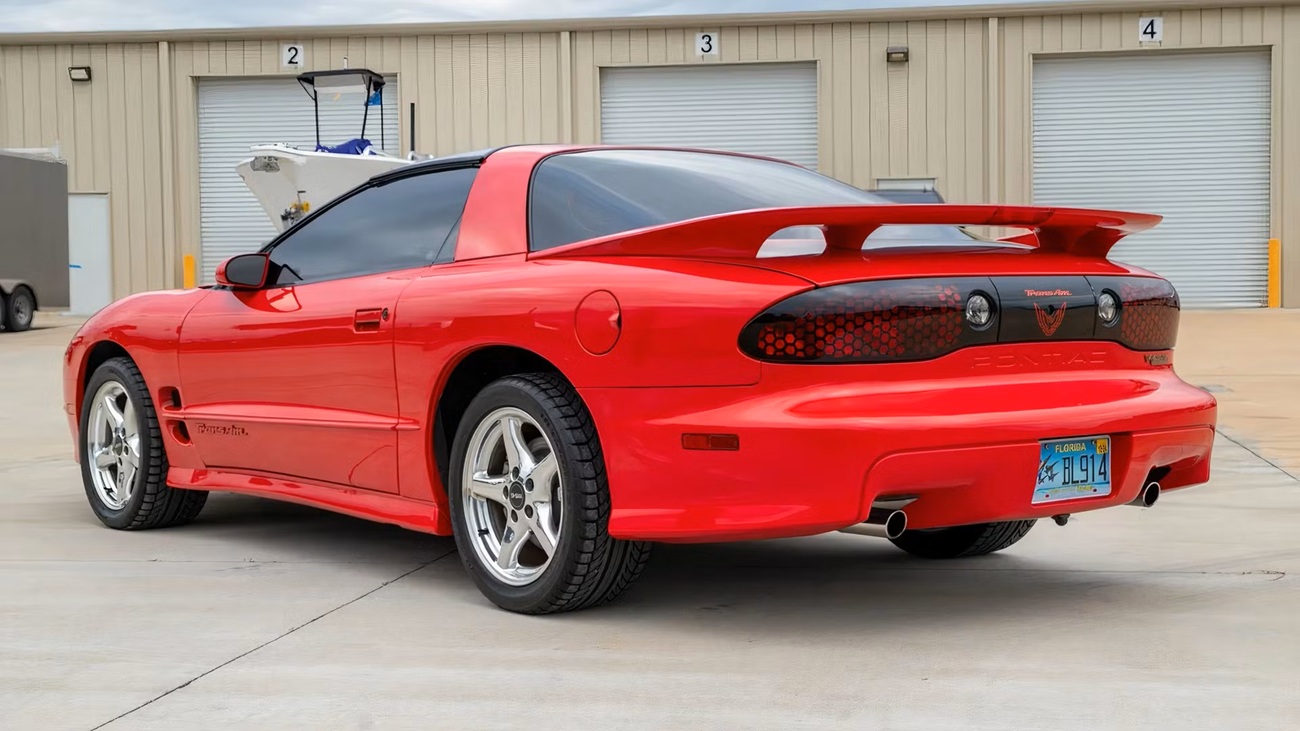 Red Pontiac Firebird Trans Am seen from the rear in a parking lot, with a large rear spoiler and Florida license plate.