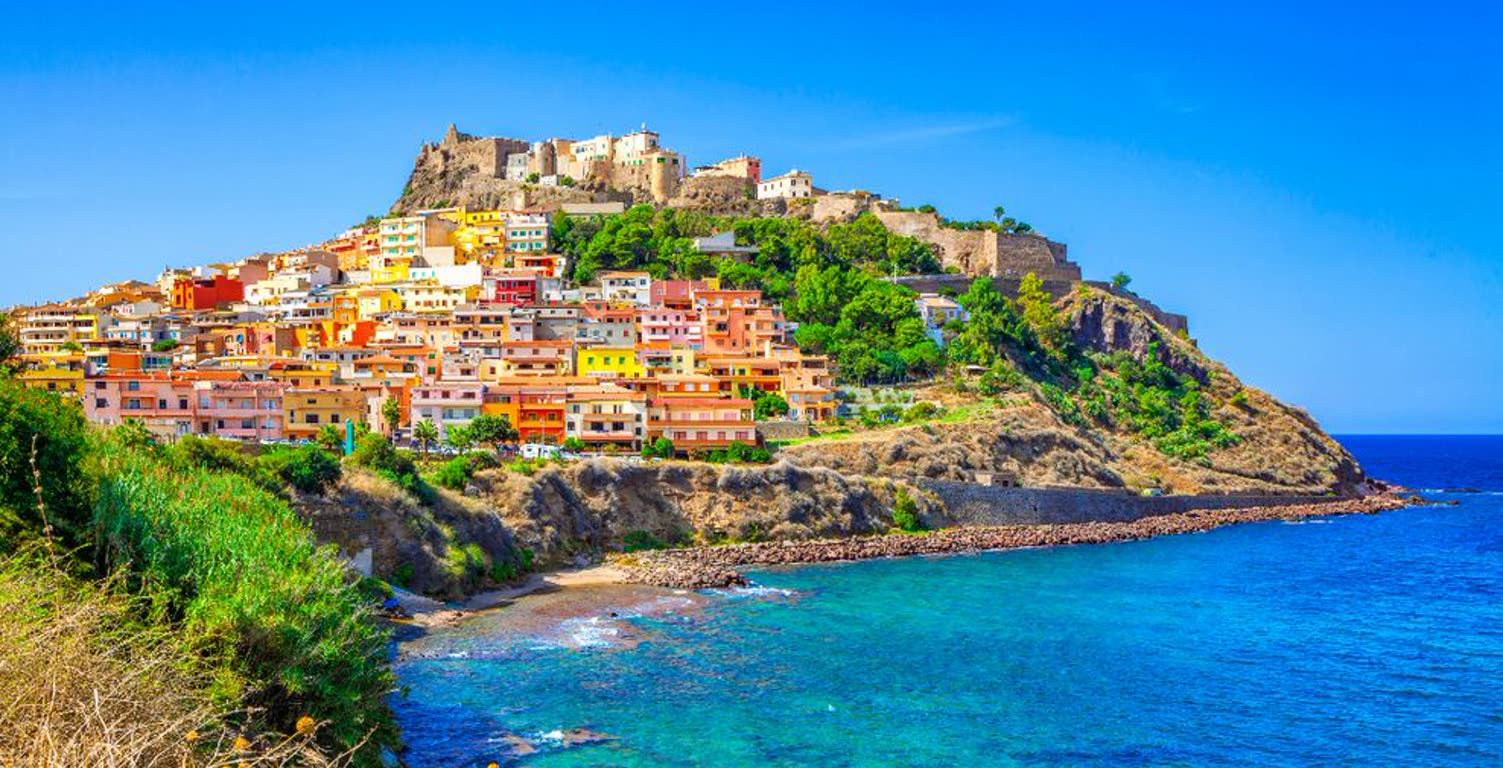 Colorful cliffside village with a fortress on top overlooking a blue bay.