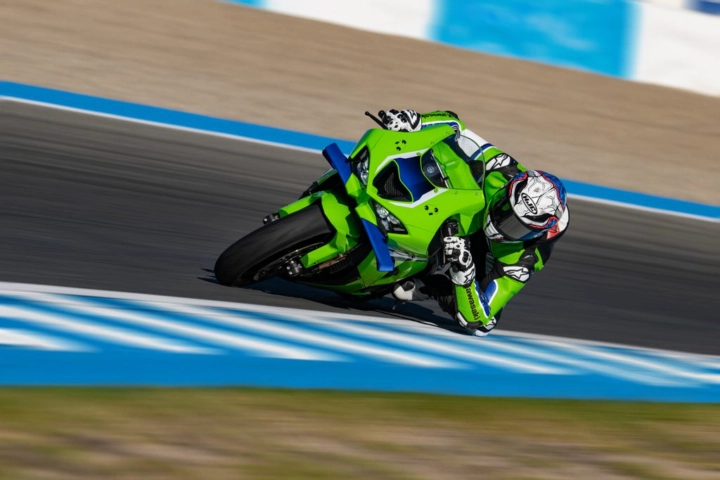 Motorcycle racer in neon green suit leaning into a turn on a race track.