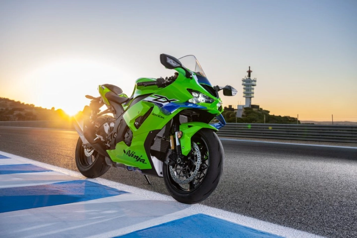 Green Kawasaki Ninja sport motorcycle on a race track at sunset, leaning on its kickstand near blue-and-white run-off lines.