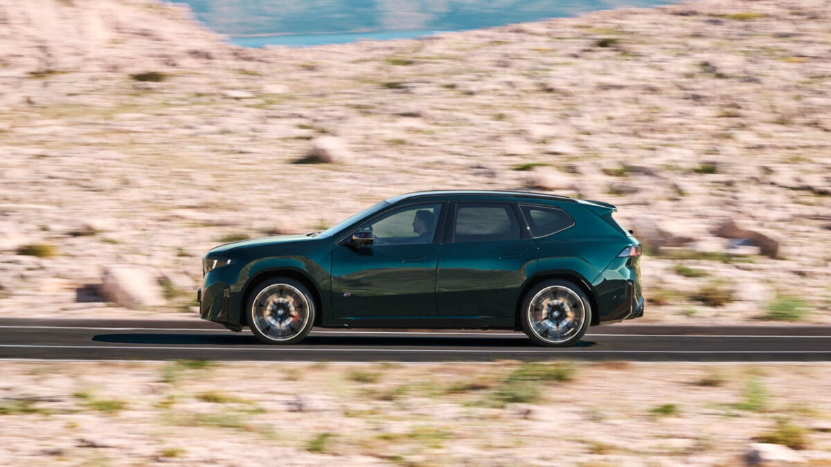 نمای جانبی شاسی‌بلند برقی BMW iX3 M60 xDrive سبز تیره با رینگ‌های آلیاژی بزرگ، سقف مشکی و طراحی آیرودینامیک در حال حرکت در جاده