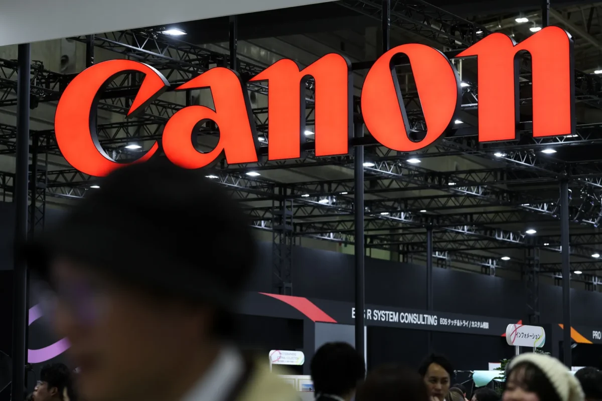 تابلوی بزرگ قرمزرنگ Canon در غرفه‌ای نمایشگاهی، بالای سر بازدیدکنندگان دیده می‌شود