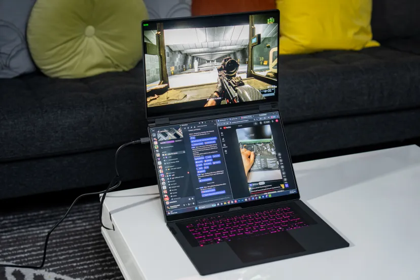 لپ‌تاپ گیمینگ ایسوس سری ROG با نورپردازی RGB کیبورد، در حال اجرای بازی شوتر در نمایشگر اصلی و برنامه‌های دیسکورد و یوتیوب در صفحه دوم.