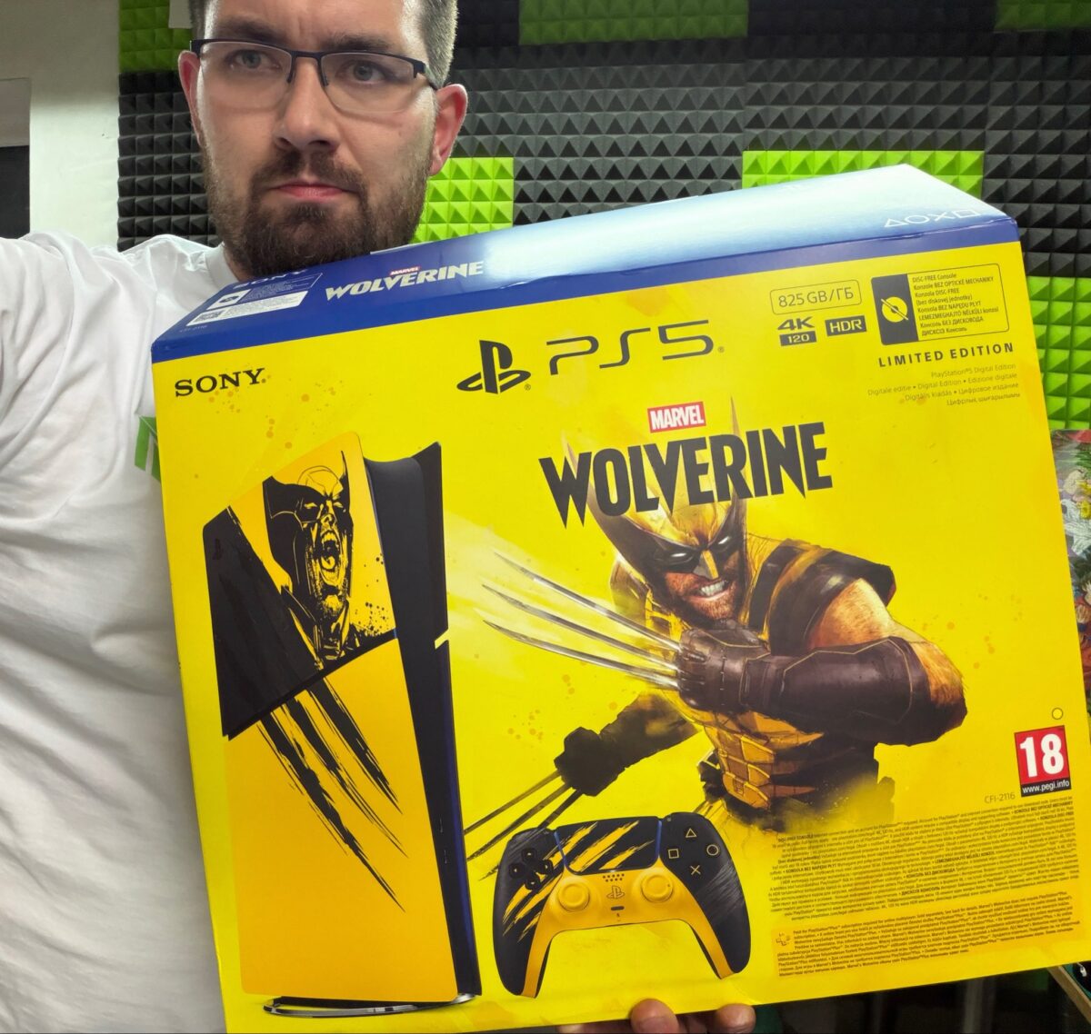 شخصی با عینک و ریش کوتاه، جعبه نسخه محدود کنسول پلی‌استیشن ۵ با طرح مارول ولورین (Marvel Wolverine) را در دست دارد؛ روی جعبه طرح ولورین با چنگال‌های معروفش به رنگ زرد و مشکی دیده می‌شود.