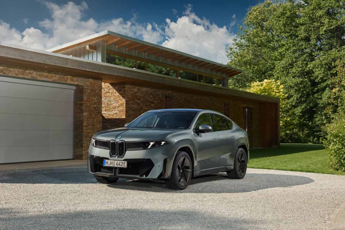 نمای سه‌رخ جلوی شاسی‌بلند برقی BMW iX4 نقره‌ای با جلوپنجره دوگانه، چراغ‌های LED باریک و سقف کوپه در مقابل خانه‌ای مدرن