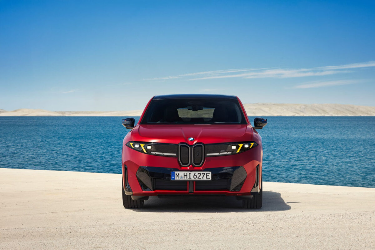 نمای روبه‌روی خودروی برقی BMW iX4 M60 قرمزرنگ با جلوپنجره دوگانه عمودی، چراغ‌های LED باریک و طراحی اسپرت در ساحل