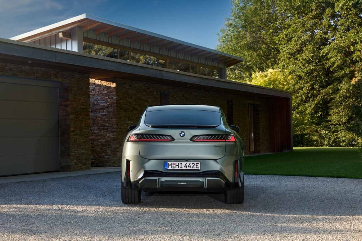 نمای مستقیم عقب BMW iX4 نقره‌ای با چراغ‌های LED افقی، نشان BMW و سپر مشکی در محوطه خانه‌ای مدرن