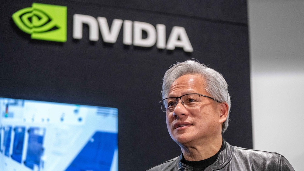 جنسن هوانگ، مدیرعامل انویدیا، با کت چرمی مشکی و عینک در حال سخنرانی در برابر لوگوی بزرگ NVIDIA