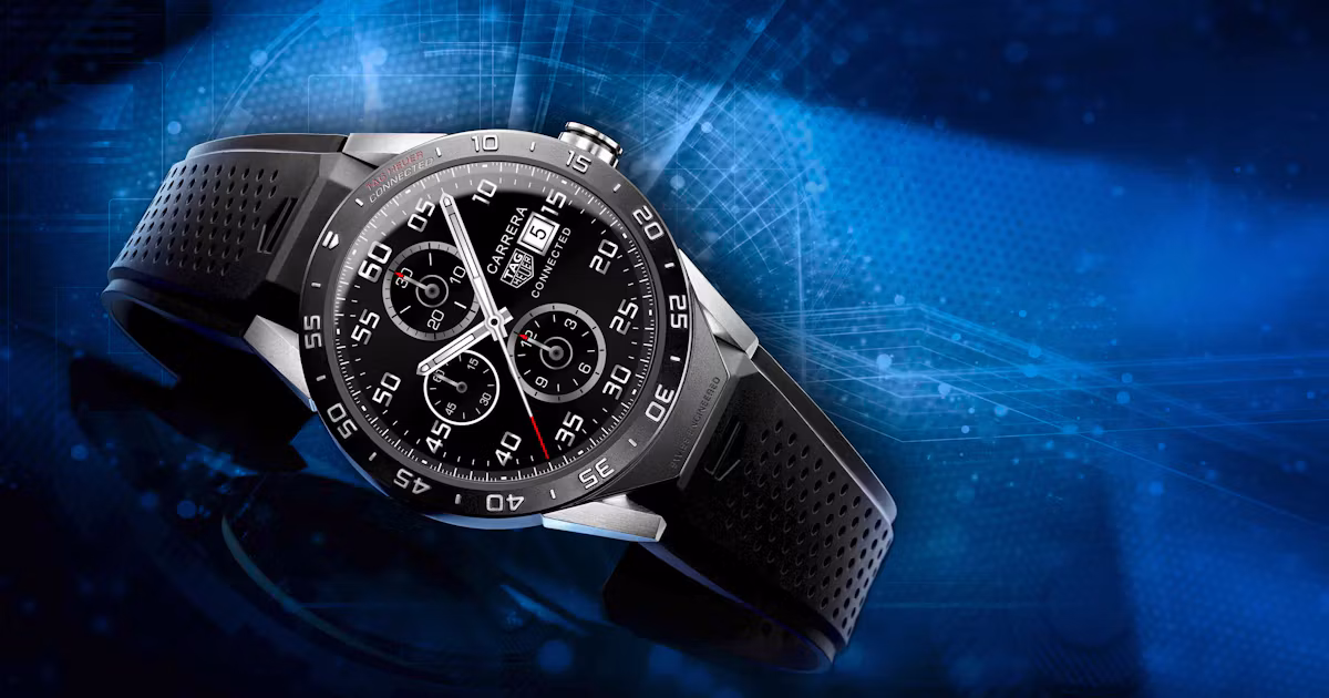 ساعت هوشمند مشکی TAG Heuer Connected با بند سیلیکونی سوراخ‌دار، صفحه کرنوگراف دیجیتال و بدنه تیتانیومی روی پس‌زمینه‌ای با طرح‌های گرافیکی آبی‌رنگ قرار دارد.