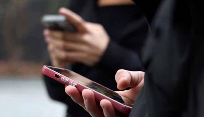 نمای نزدیک از دست دو فرد در حال استفاده و تایپ با گوشی‌های هوشمند با کاورهای صورتی و مشکی