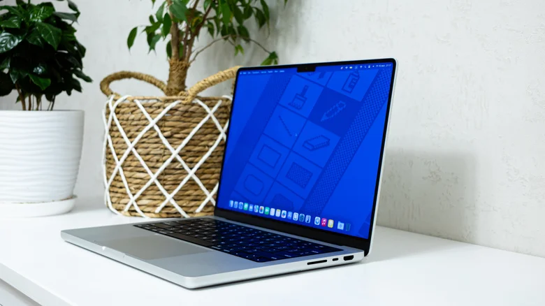 یک MacBook Pro باز روی میز سفید قرار دارد و صفحه‌نمایش آن رابط کاربری macOS را نشان می‌دهد.