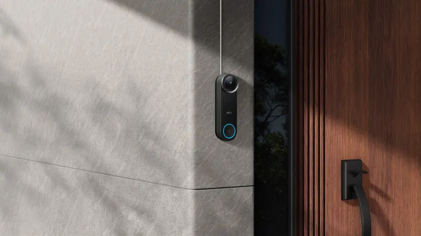 زنگ ویدیویی هوشمند یوفی مدل Video Doorbell S4 با کلید دارای نور آبی، نصب‌شده روی دیوار سنگی در کنار درب ورودی چوبی خانه.