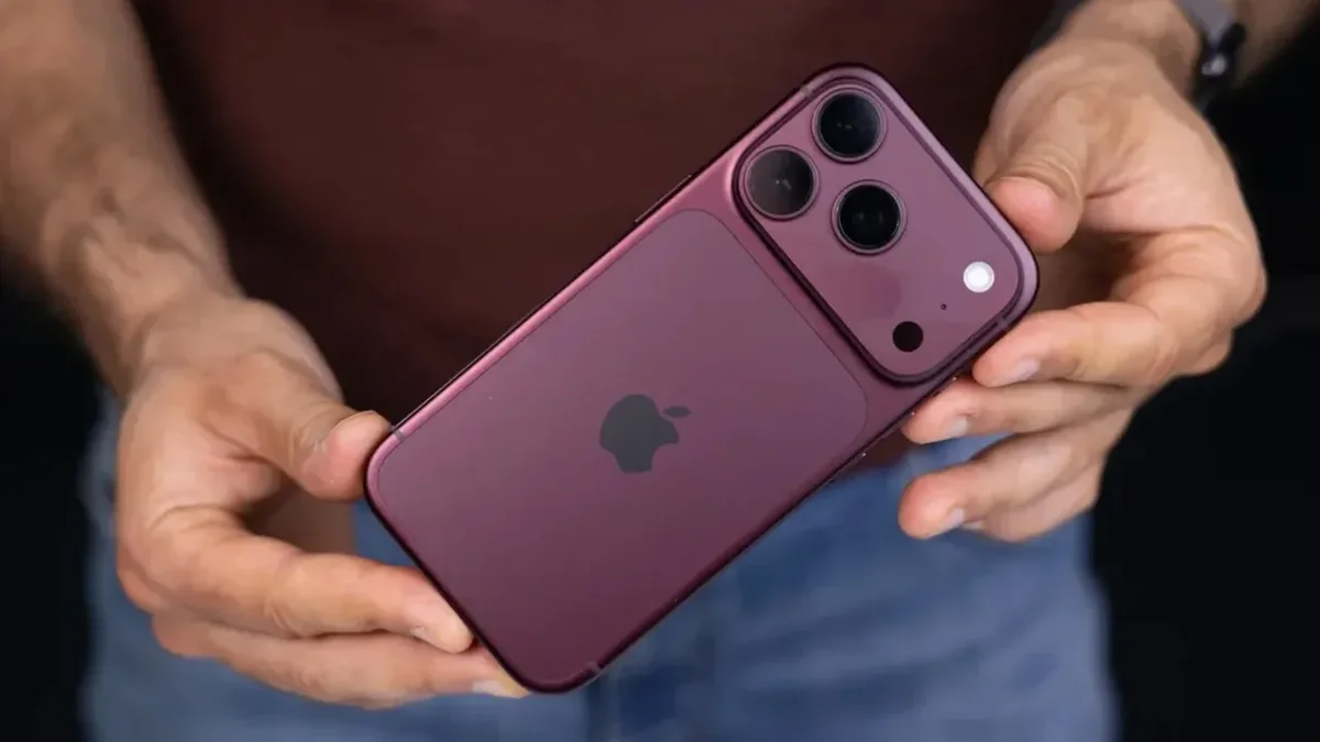 یک iPhone 18 Pro به رنگ بنفش تیره در دست گرفته شده و نمای پشت دستگاه با سه لنز دوربین، لوگوی Apple و فلاش دوربین را نشان می‌دهد.