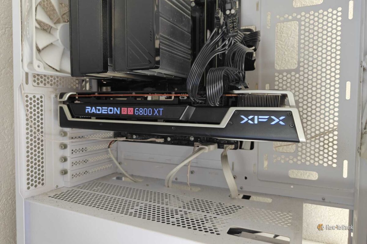 نمای داخلی کیس کامپیوتر سفید رنگ که کارت گرافیک XFX Radeon RX 6800 XT را با نورپردازی آبی لوگوی XFX در کنار فن‌های سفیدِ خنک‌کننده پردازنده نشان می‌دهد.