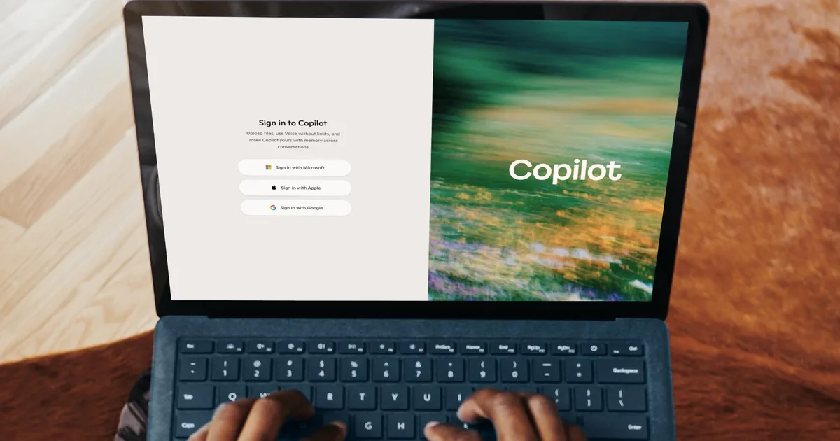دست‌ها در حال تایپ روی لپ‌تاپ Microsoft Surface با صفحه‌ی ورود به سایت Microsoft Copilot شامل گزینه‌های ورود با Microsoft، Apple و Google