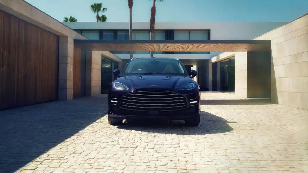 شاسی‌بلند استون مارتین (Aston Martin) DBX با بدنه بنفش در مقابل یک ویلای مدرن