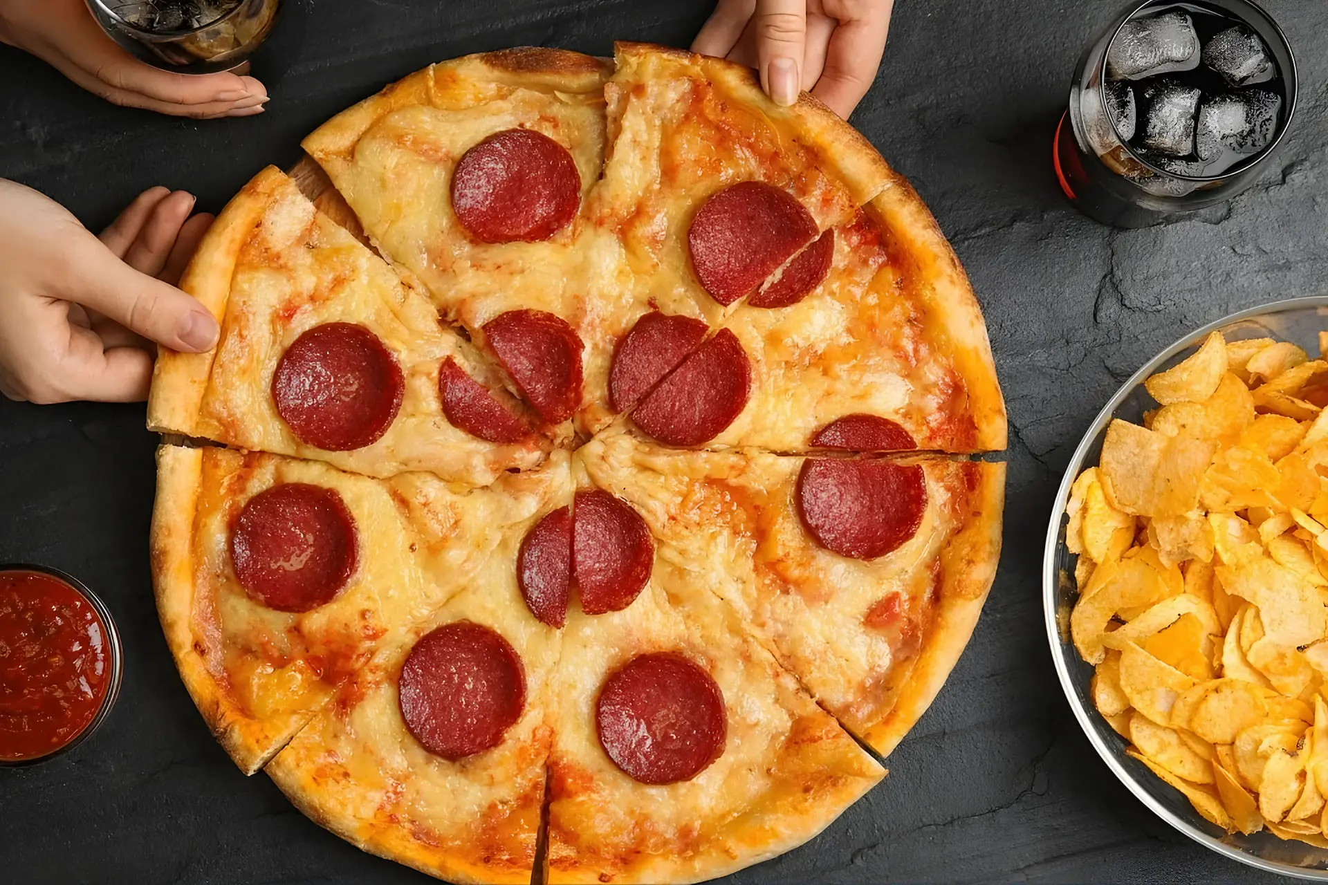 پیتزای پپرونی (Pepperoni) و ظرف چیپس روی میز در کنار نوشیدنی