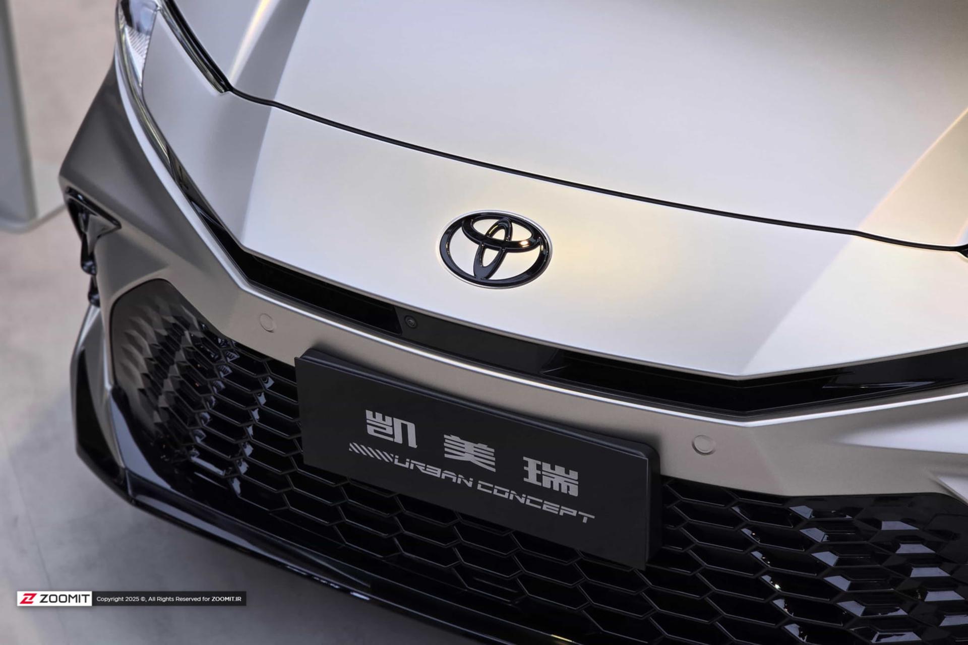 لوگوی برند تویوتا (Toyota) روی بدنه نقره‌ای خودروی هیبریدی