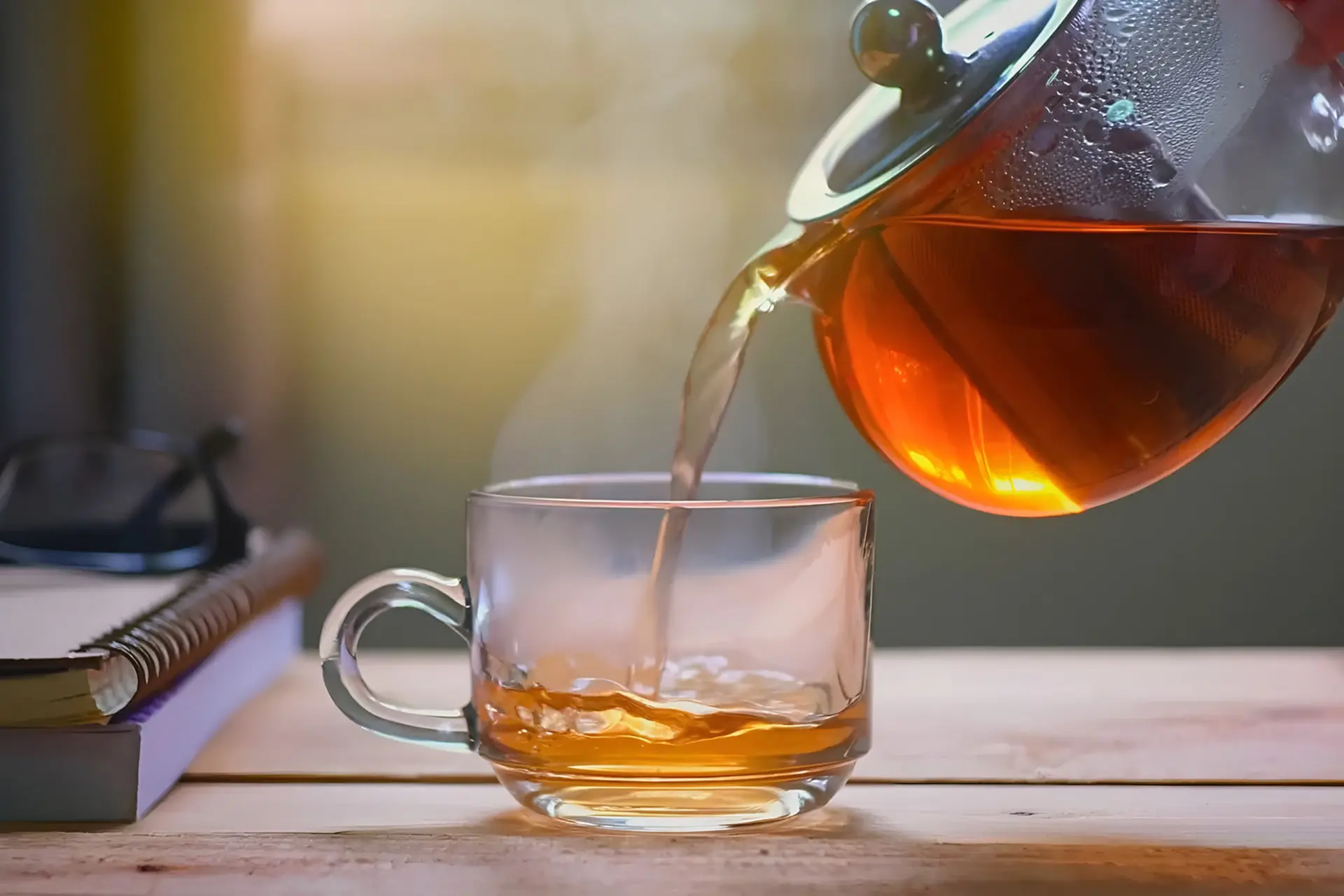 ریختن چای داغ از قوری شیشه‌ای درون فنجان شفاف