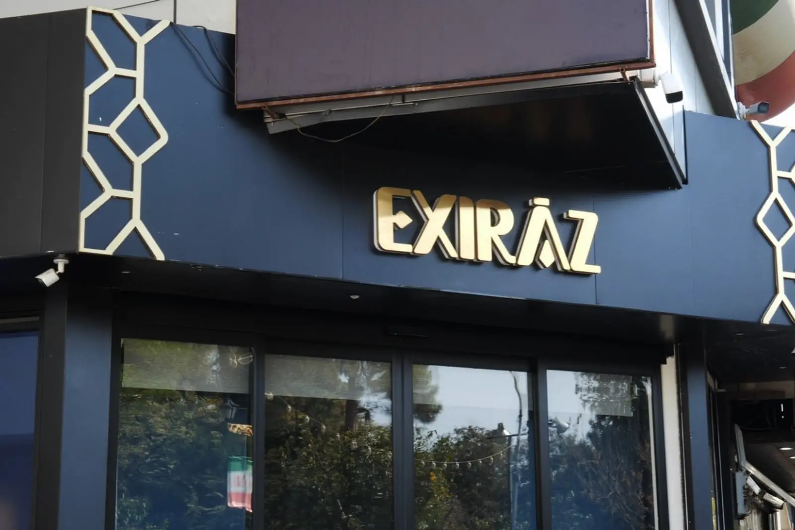 نمای تابلوی طلایی رنگ فروشگاه اکسیراز (Exiraz) روی نمای سیاه ساختمان